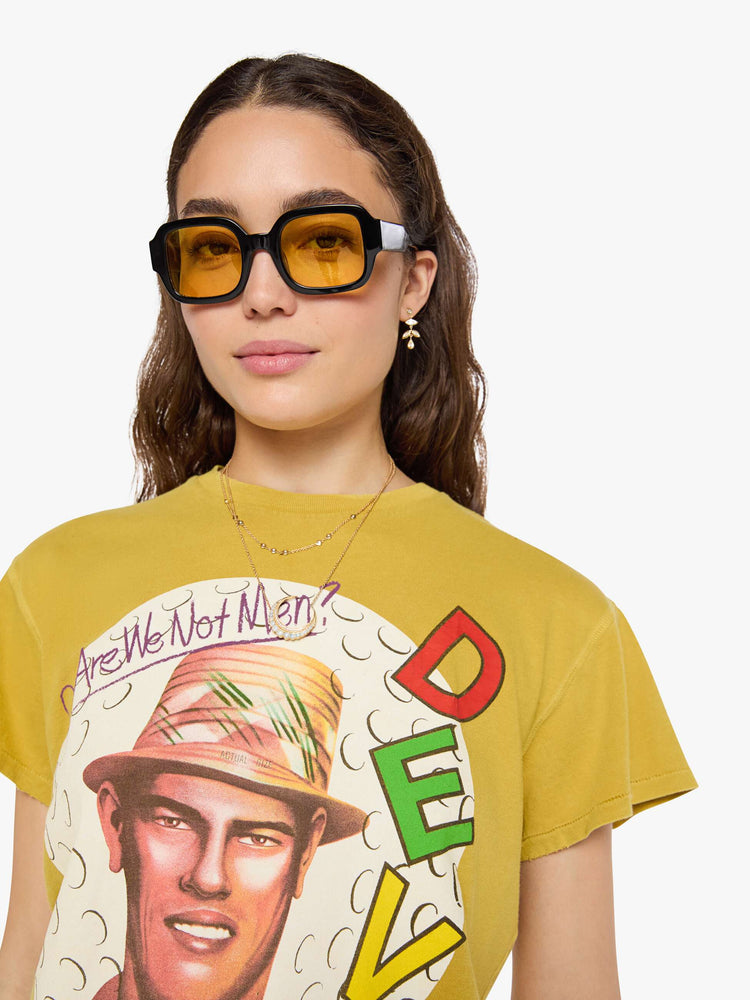 Close up  view of a woman in a yellow yellow the tee honors Devo with a graphic portrait and colorful text on the front.