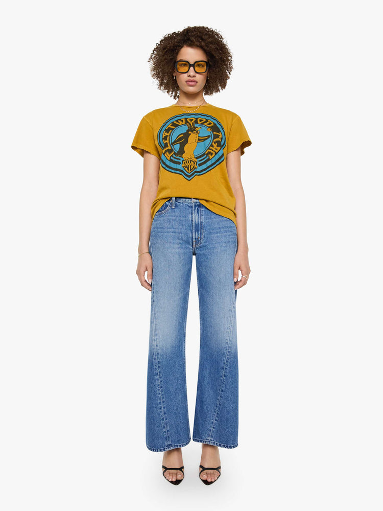 Full body view of a woman in a mustard yellow tee that pays homage to Fleetwood Mac with a colorful penguin portrait and text on the front.