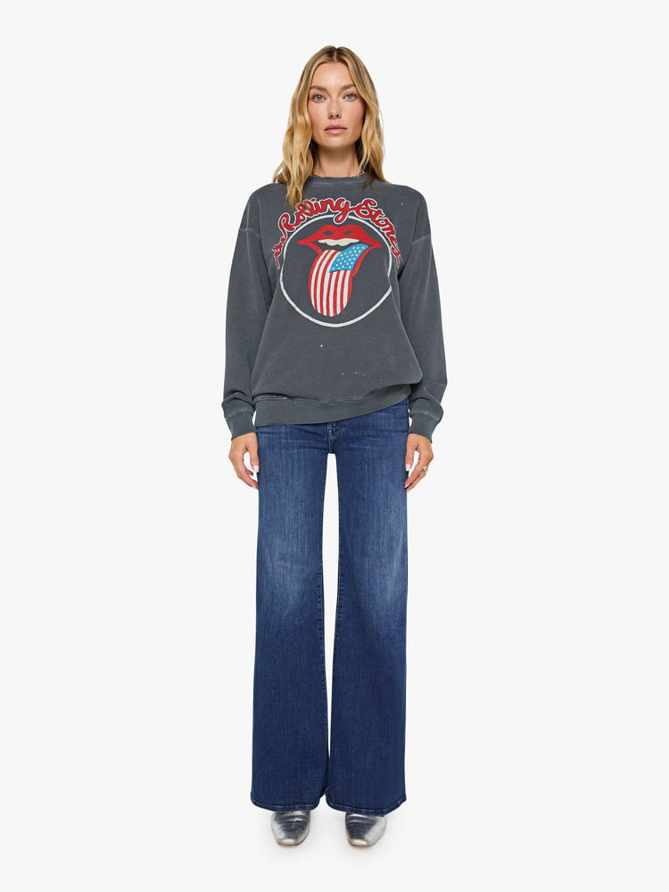 Full body view of a woman in dark grey sweatshirt pays homage to The Rolling Stones with the band's iconic tongue graphic on the front.