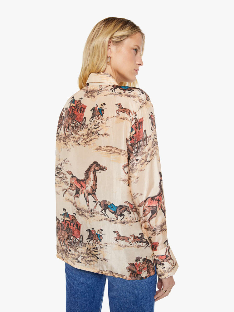 Back view of a woman in a button up peachy cream with cowboy motifs, and features long balloon sleeves and a loose fit.