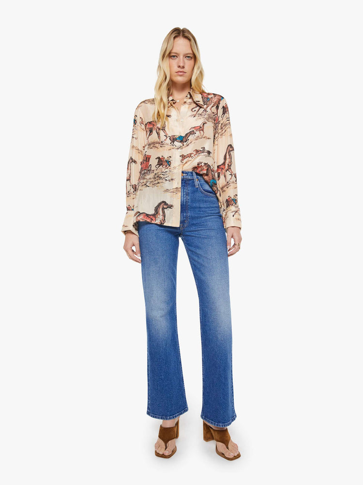 Full body view of a woman in a button up peachy cream with cowboy motifs, and features long balloon sleeves and a loose fit.