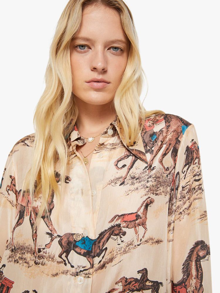 Close up view of a woman in a button up peachy cream with cowboy motifs, and features long balloon sleeves and a loose fit.