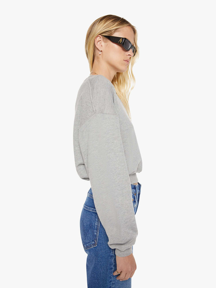 Side view of woman in a grey with the brand's logo embroidered on the chest in white, the crewneck sweatshirt is designed with ribbed hems and a cropped, cozy fit.