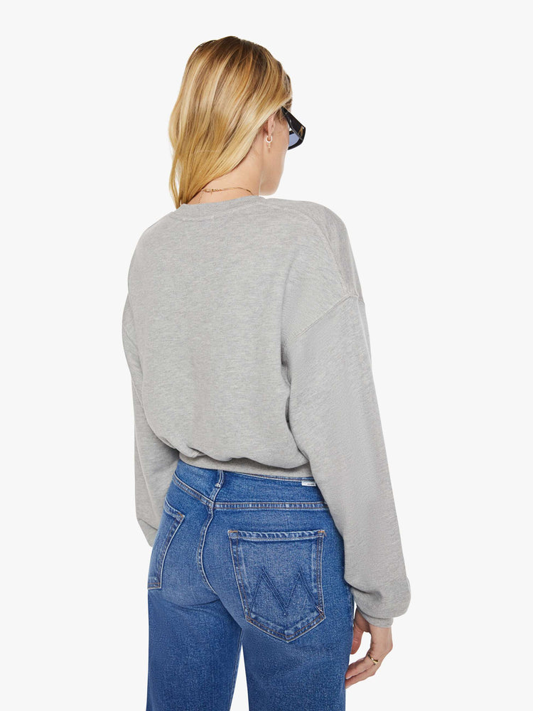 Back view of woman in a grey with the brand's logo embroidered on the chest in white, the crewneck sweatshirt is designed with ribbed hems and a cropped, cozy fit.
