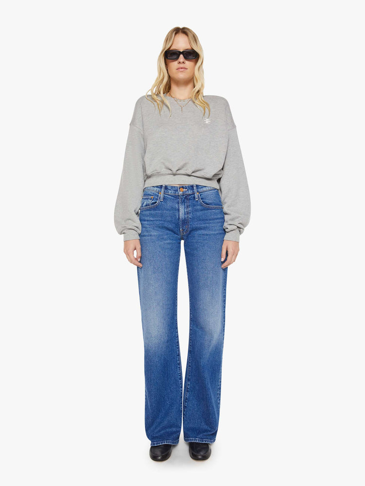Full body view of woman in a grey with the brand's logo embroidered on the chest in white, the crewneck sweatshirt is designed with ribbed hems and a cropped, cozy fit.