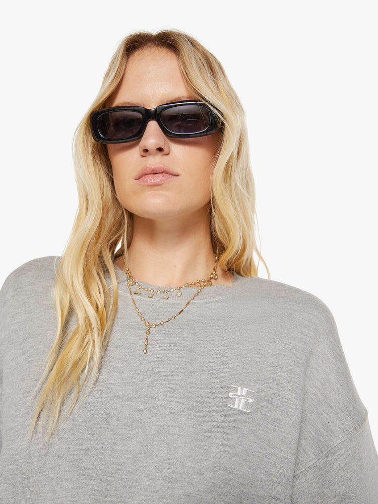 Close up view of woman in a grey with the brand's logo embroidered on the chest in white, the crewneck sweatshirt is designed with ribbed hems and a cropped, cozy fit.