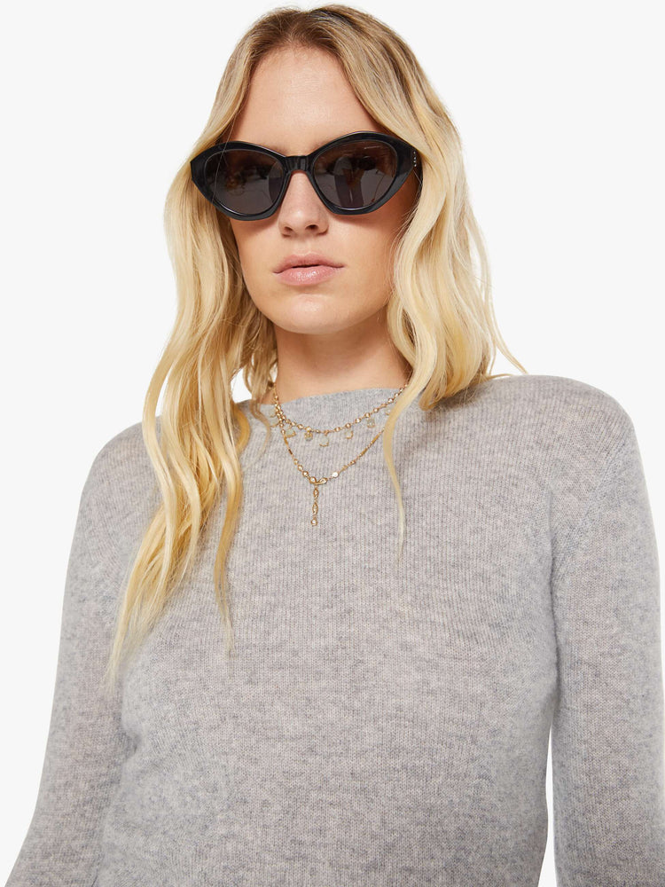 Close up view of a woman in a grey sweater is designed with ribbed hems and a cropped fit.