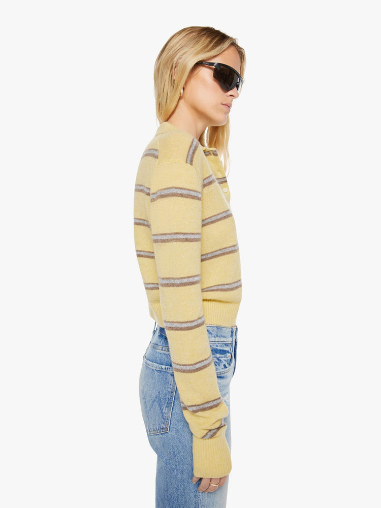 Side view of a woman in a butter yellow sweater with horizontal blue stripes, the sweater is designed with a buttoned neck, long sleeves, ribbed hems and a cropped fit. 