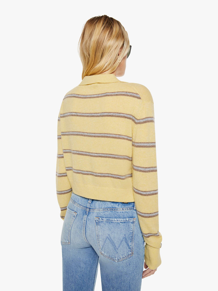 Back view of a woman in a butter yellow sweater with horizontal blue stripes, the sweater is designed with a buttoned neck, long sleeves, ribbed hems and a cropped fit. 