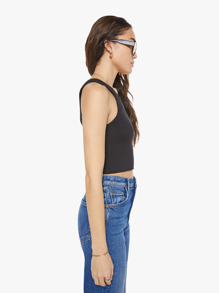 Side view of a woman in a black scoop neck tank is designed with a cropped fit.