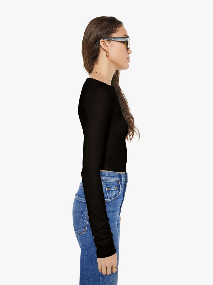 Side view of a woman in a black boatneck top has extra-long sleeves and a narrow fit.