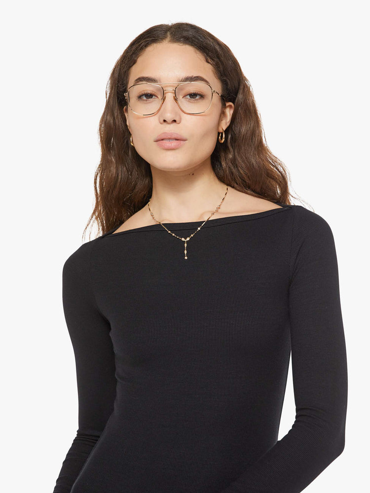 Close up view of a woman in a black boatneck mini dress is designed with long sleeves, a thigh-length hem and narrow fit.
