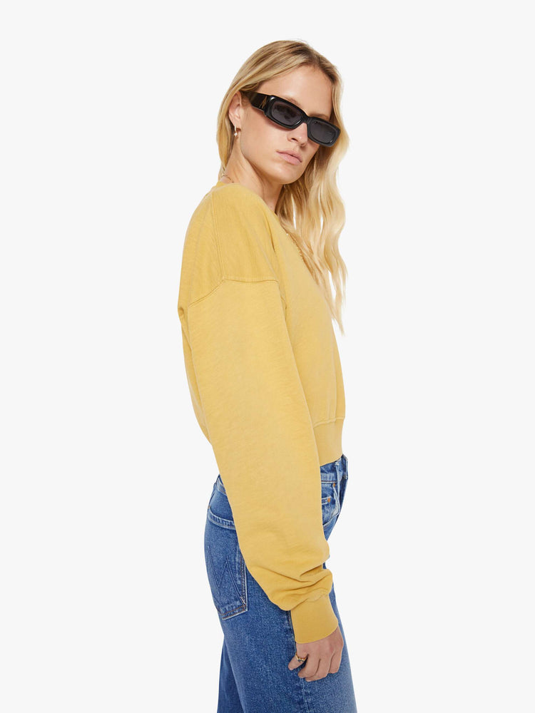 Side view of a woman in a yellow  sweatshirt with a short V-neck, drop shoulders, ribbed hems and a cropped, cozy fit. 