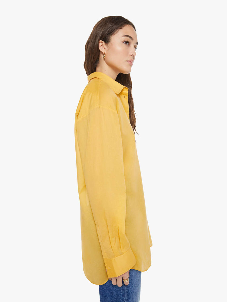 Side view of a woman in a golden yellow oversized button-up shirt.