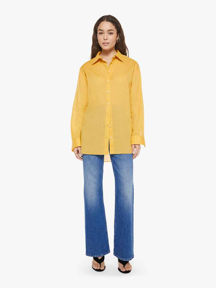 Full body view of a woman in a golden yellow oversized button-up shirt.
