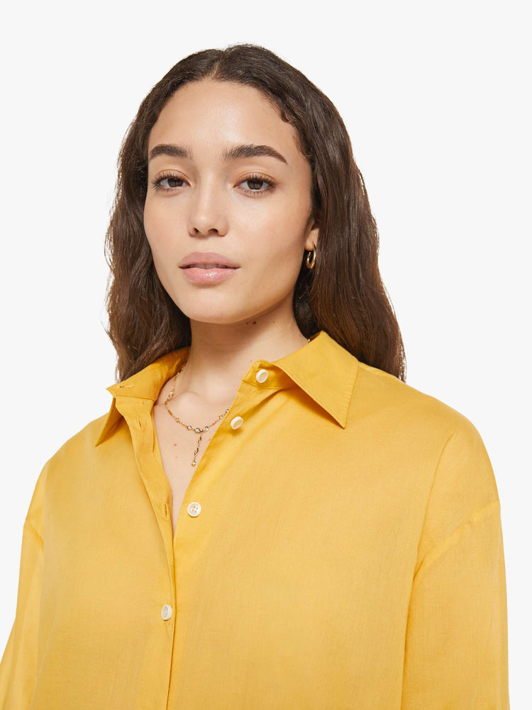 Close up view of a woman in a golden yellow oversized button-up shirt.