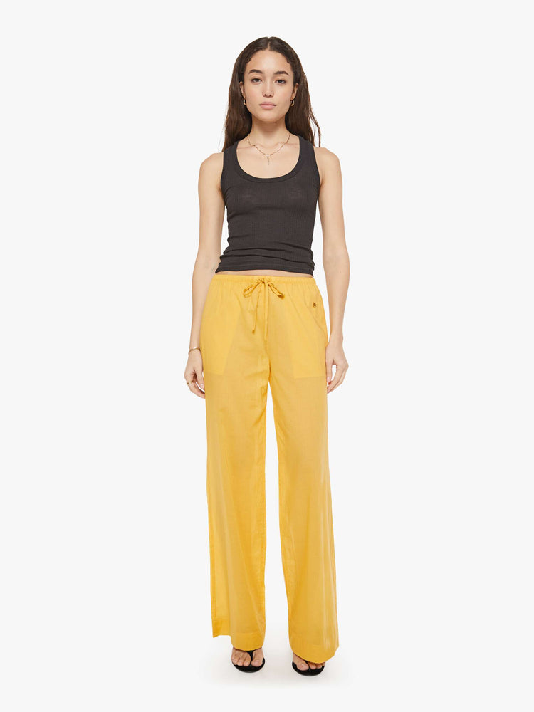 Front view of a woman in a yellow pant designed with a drawstring waistband, slit pockets, wide leg and a loose fit.
