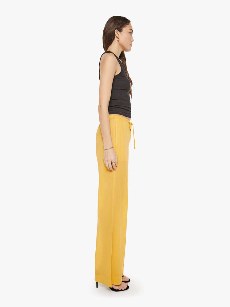 Side view of a woman in a yellow pant designed with a drawstring waistband, slit pockets, wide leg and a loose fit.