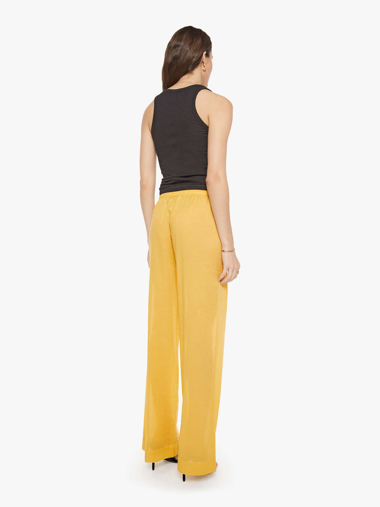 Back view of a woman in a yellow pant designed with a drawstring waistband, slit pockets, wide leg and a loose fit.