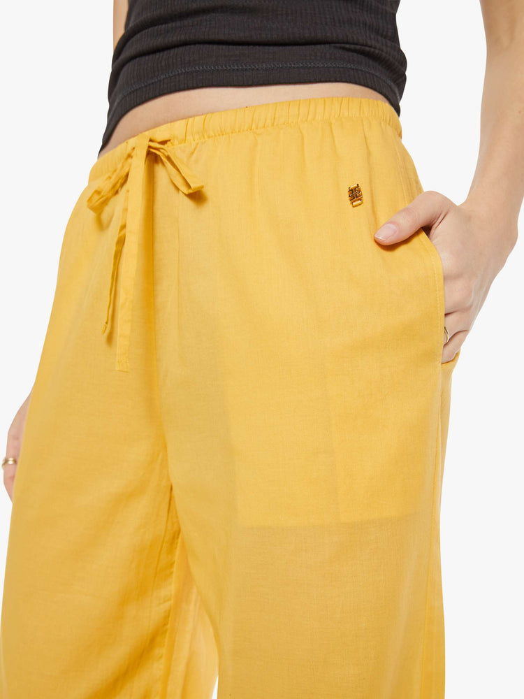 Close up view of a woman in a yellow pant designed with a drawstring waistband, slit pockets, wide leg and a loose fit.