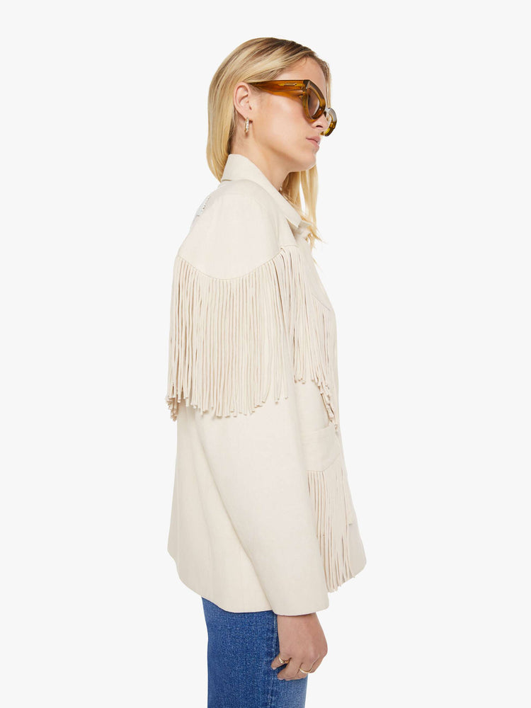 Side view of a woman in a cream with fringe details jacket it has slightly dropped shoulders, front patch pockets, buttons down the front and a boxy fit.