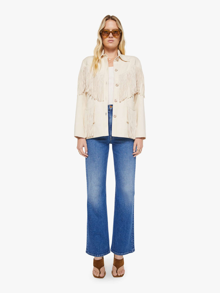 Full body view of a woman in a cream with fringe details jacket it has slightly dropped shoulders, front patch pockets, buttons down the front and a boxy fit.