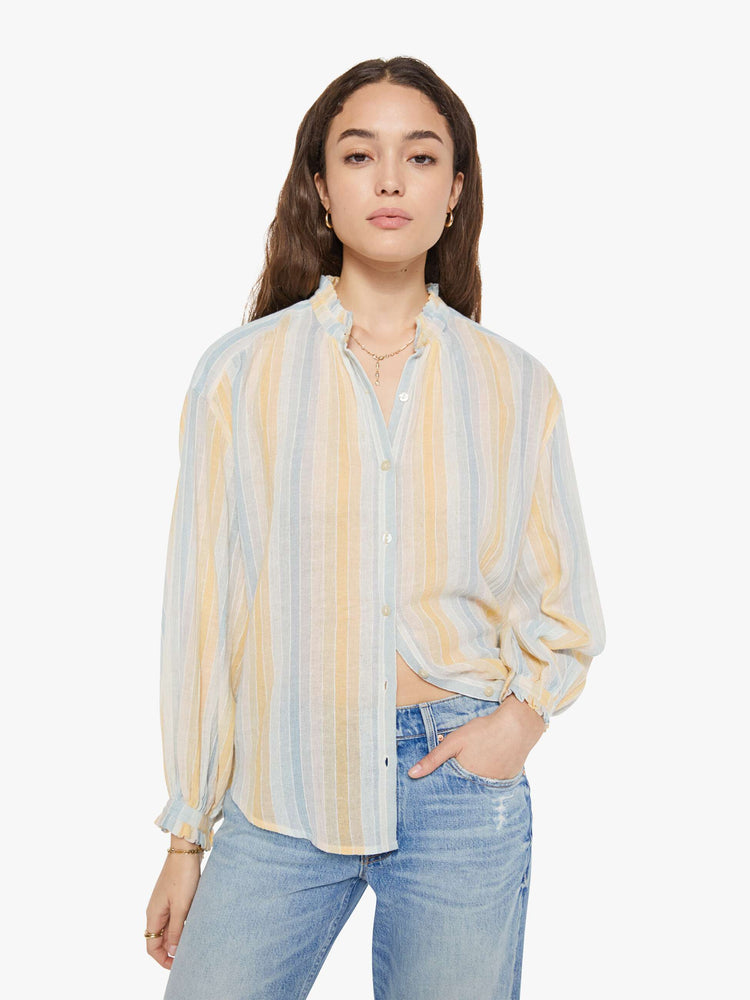 Front view of a woman in a vertical yellow, white and light blue stripes, and features a stacked collar shirt, drop shoulders, long balloon sleeves and a curved hem.