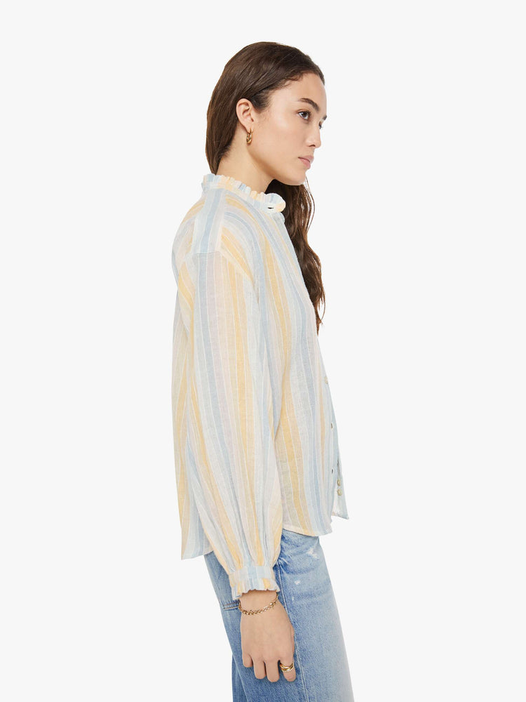 Side view of a woman in a vertical yellow, white and light blue stripes, and features a stacked collar shirt, drop shoulders, long balloon sleeves and a curved hem.