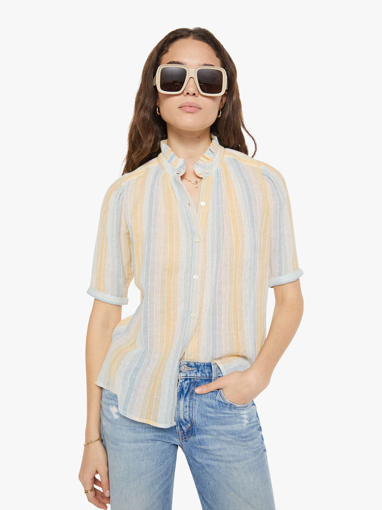 Front view of a woman in a vertical yellow, white and light blue stripes, and features a stacked collar shirt with an elbow-length sleeves, buttons down the front and a curved hem.