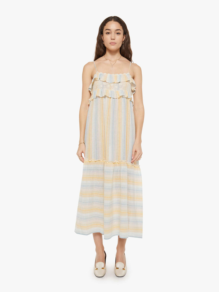 Front view of a woman in a vertical yellow, white and light blue stripes dress with thin spaghetti straps, a square neck with ruffles, a loose, tiered skirt and an ankle-length hem.