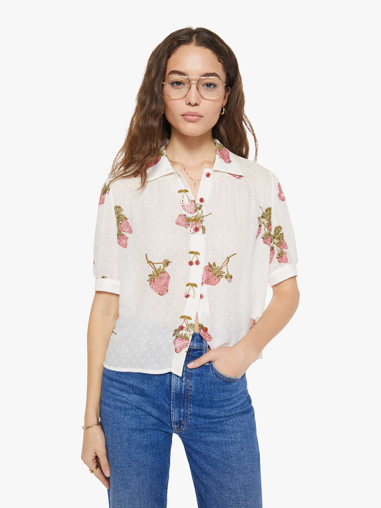 Front view of a woman in an off-white shirt with a faded strawberry print, and is designed with a collared neck, short sleeves and buttons down the front.