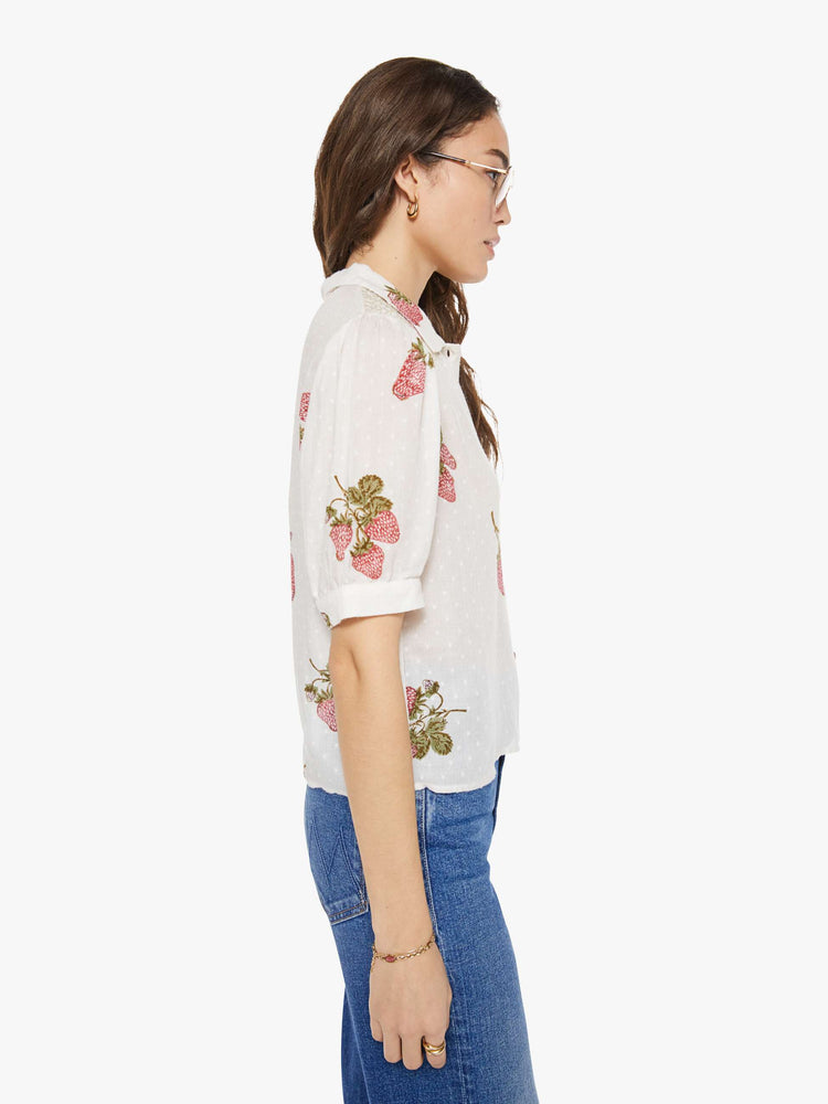 Side view of a woman in an off-white shirt with a faded strawberry print, and is designed with a collared neck, short sleeves and buttons down the front.