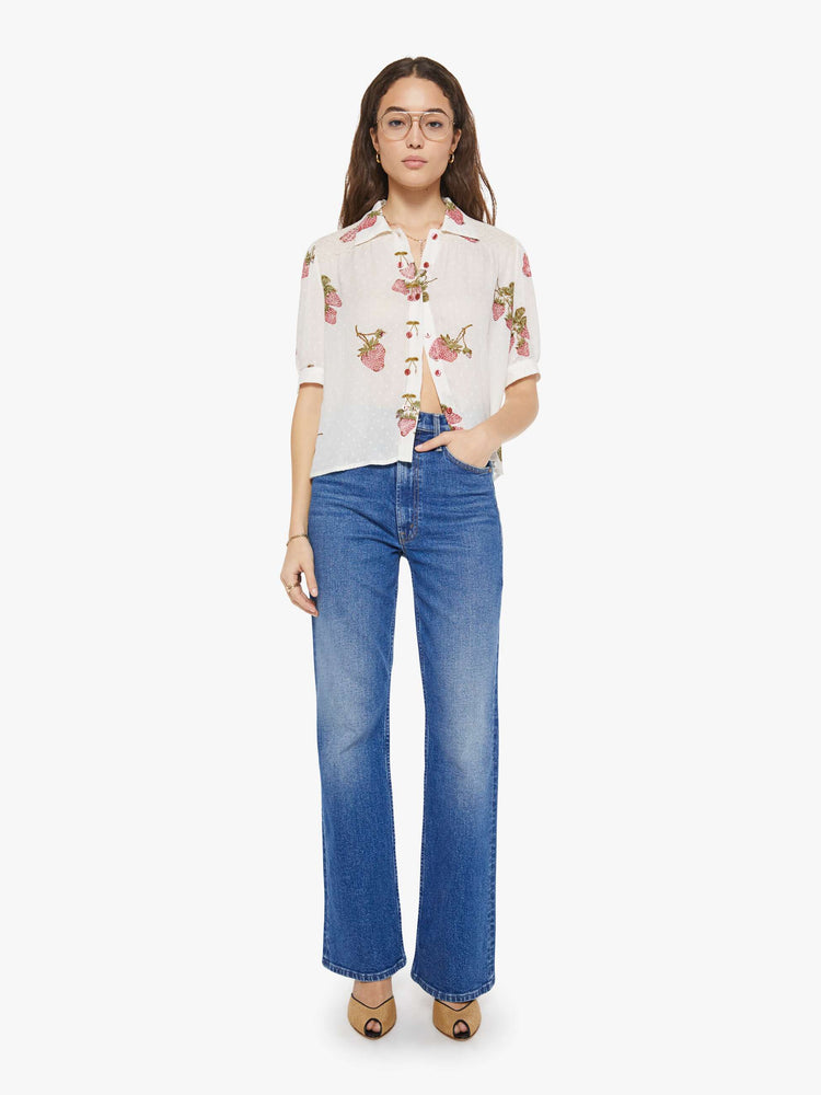 Full body view of a woman in an off-white shirt with a faded strawberry print, and is designed with a collared neck, short sleeves and buttons down the front.