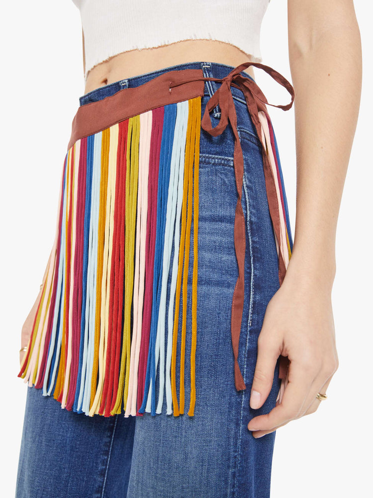 Close up view of a woman in fringe mini skirt is made from 100% silk in colorful vertical stripes and features a side tie closure and thigh-length hem. Wear it over your favorite MOTHER jeans.