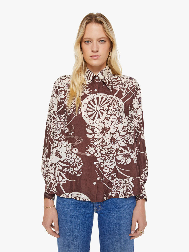 Front view of a woman in a brown with a white vintage-inspired print shirt that features drop shoulders, long sleeves, curved hems and buttons down the front.