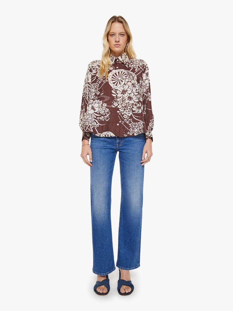 Full body view of a woman in a brown with a white vintage-inspired print shirt that features drop shoulders, long sleeves, curved hems and buttons down the front.