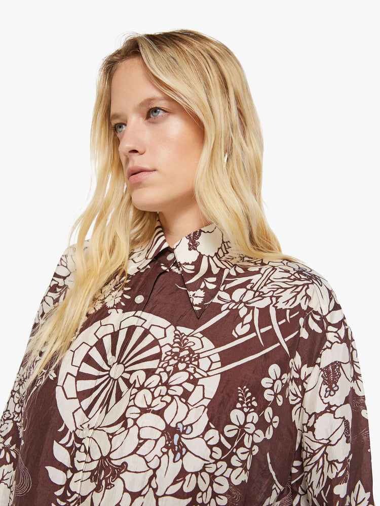 Close up view of a woman in a brown with a white vintage-inspired print shirt that features drop shoulders, long sleeves, curved hems and buttons down the front.