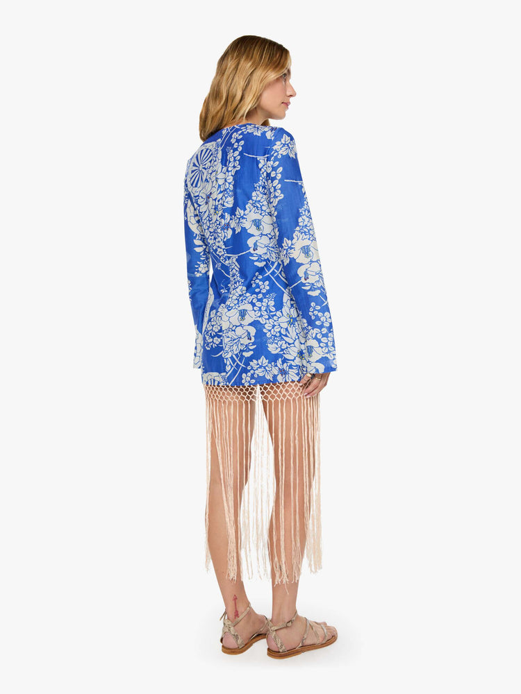 Back view of a woman in a blue with a white vintage-inspired print dress and features a crewneck, long sleeves and fringe that hits at the ankle.