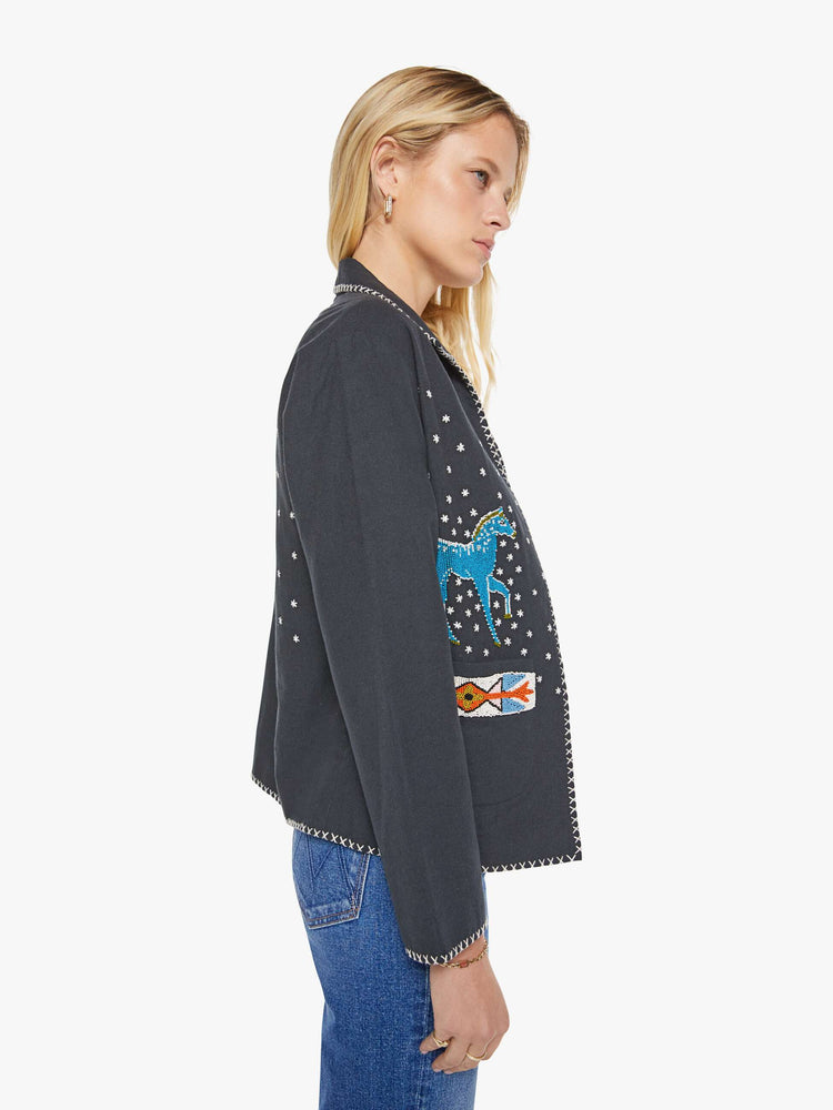Side view of a woman in a  faded grey jacket features horse motifs throughout. It has slightly dropped shoulders, front patch pockets and a tailored fit that hugs the body like a blazer. 