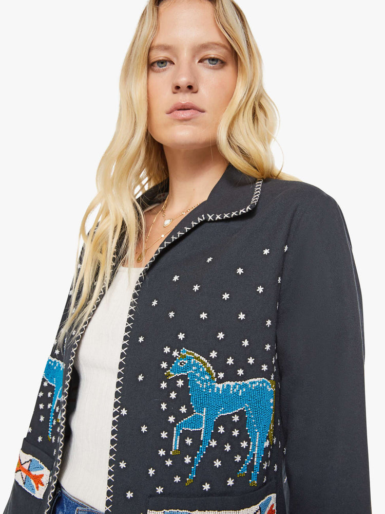 Close up view of a woman in a  faded grey jacket features horse motifs throughout. It has slightly dropped shoulders, front patch pockets and a tailored fit that hugs the body like a blazer. 