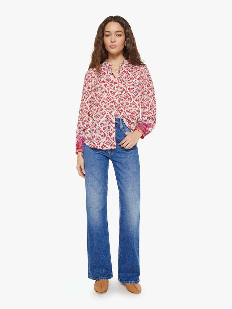 Full body view of a woman in cream and pink graphic print buttoned V-neck blouse  and a loose fit.