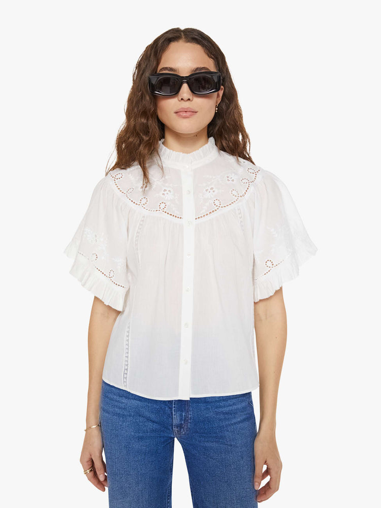 Front view of a woman in a white short sleeve with embroidery and eyelet details on the chest and sleeves.