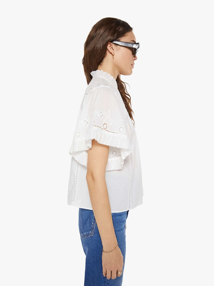 Side view of a woman in a white short sleeve with embroidery and eyelet details on the chest and sleeves.