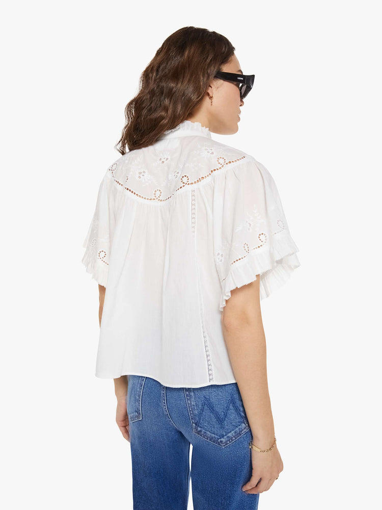 Back view of a woman in a white short sleeve with embroidery and eyelet details on the chest and sleeves.