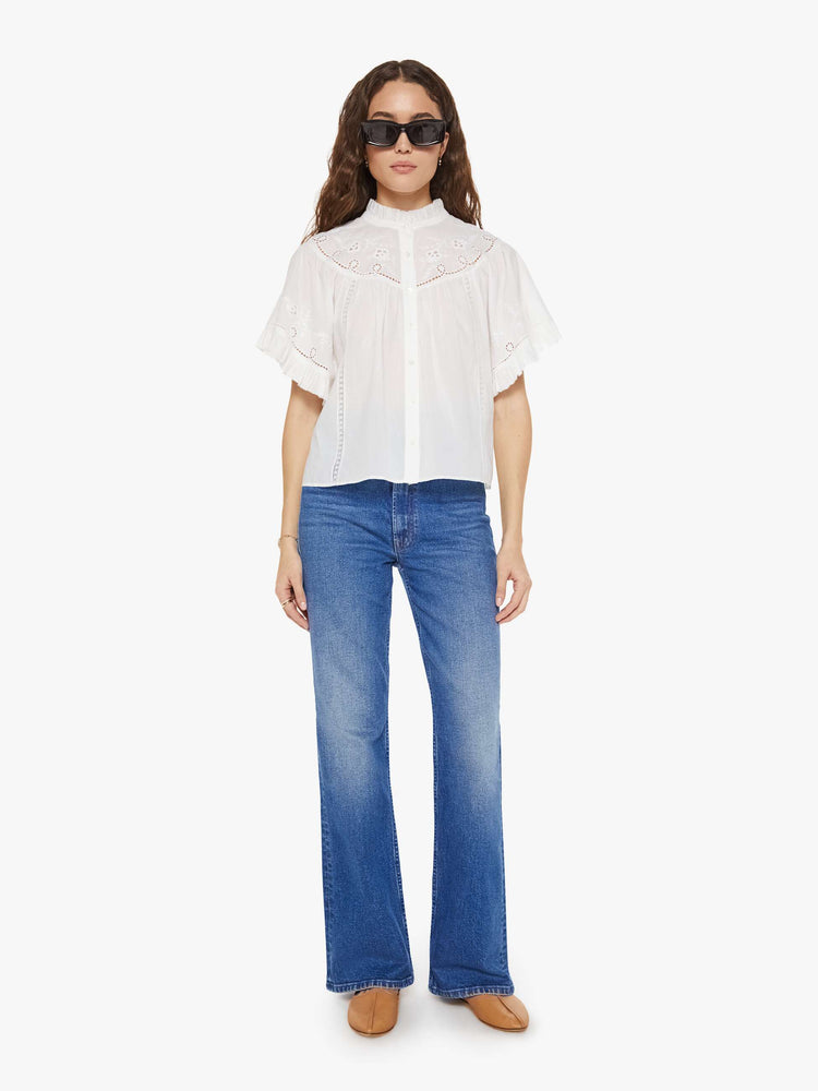 Full body view of a woman in a white short sleeve with embroidery and eyelet details on the chest and sleeves.