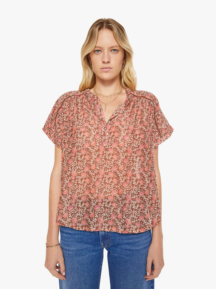 Front view of a woman in a buttoned V-neck, short sleeves and a loose, flowy fit floral print shirt.