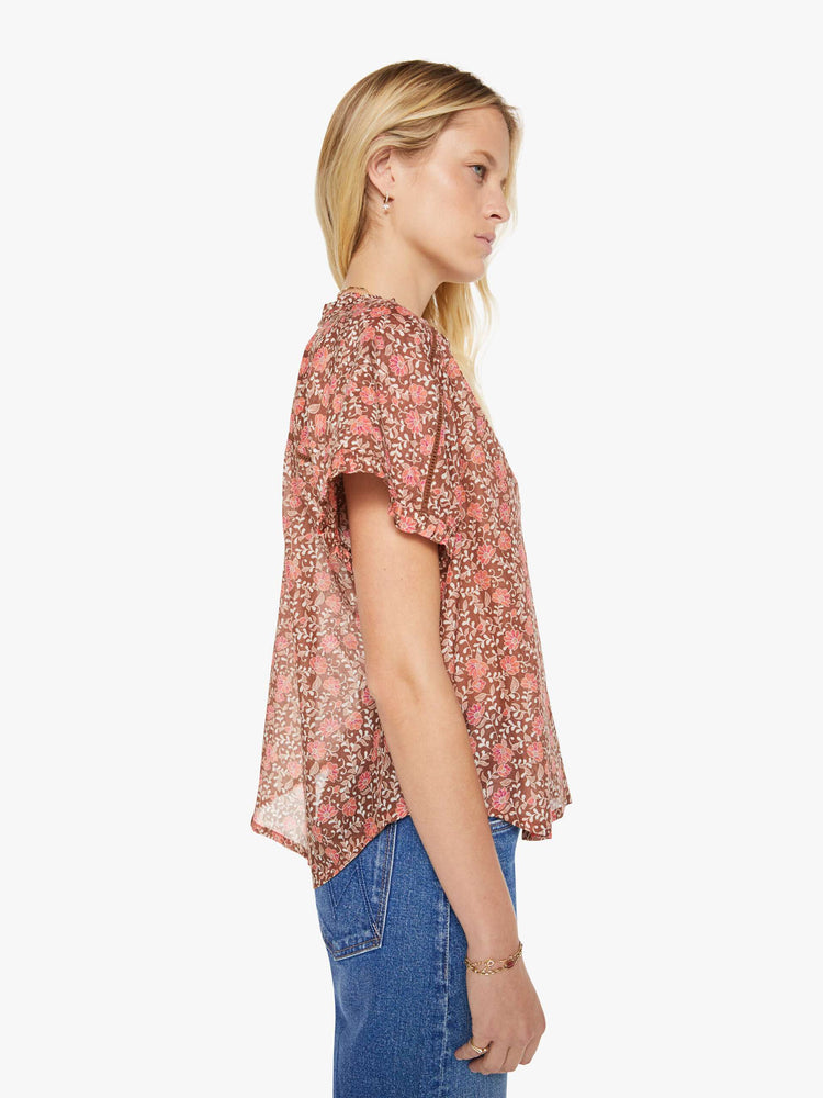 Side view of a woman in a buttoned V-neck, short sleeves and a loose, flowy fit floral print shirt.