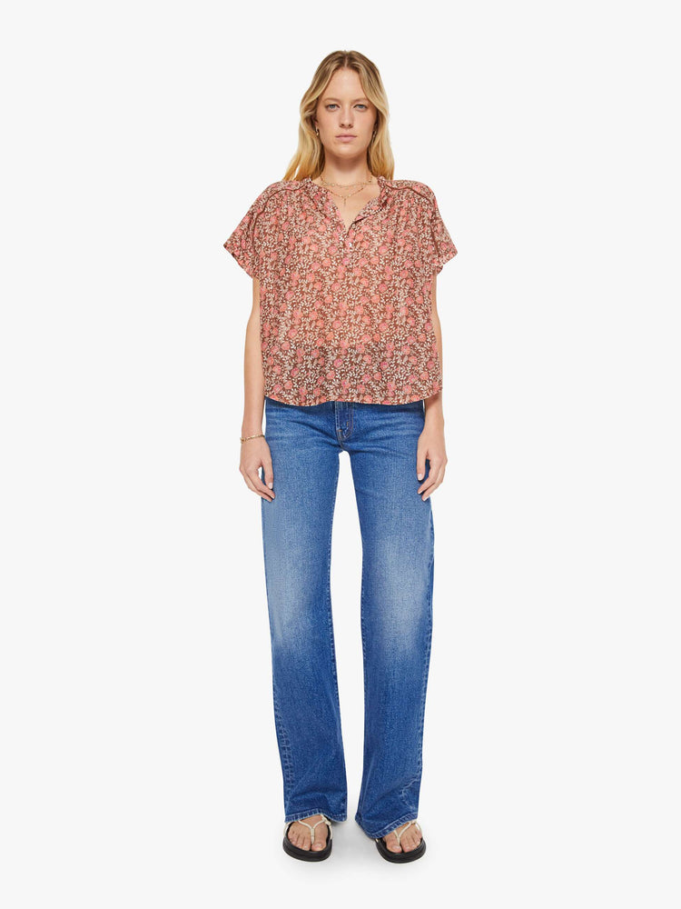 Full body view of a woman in a buttoned V-neck, short sleeves and a loose, flowy fit floral print shirt.