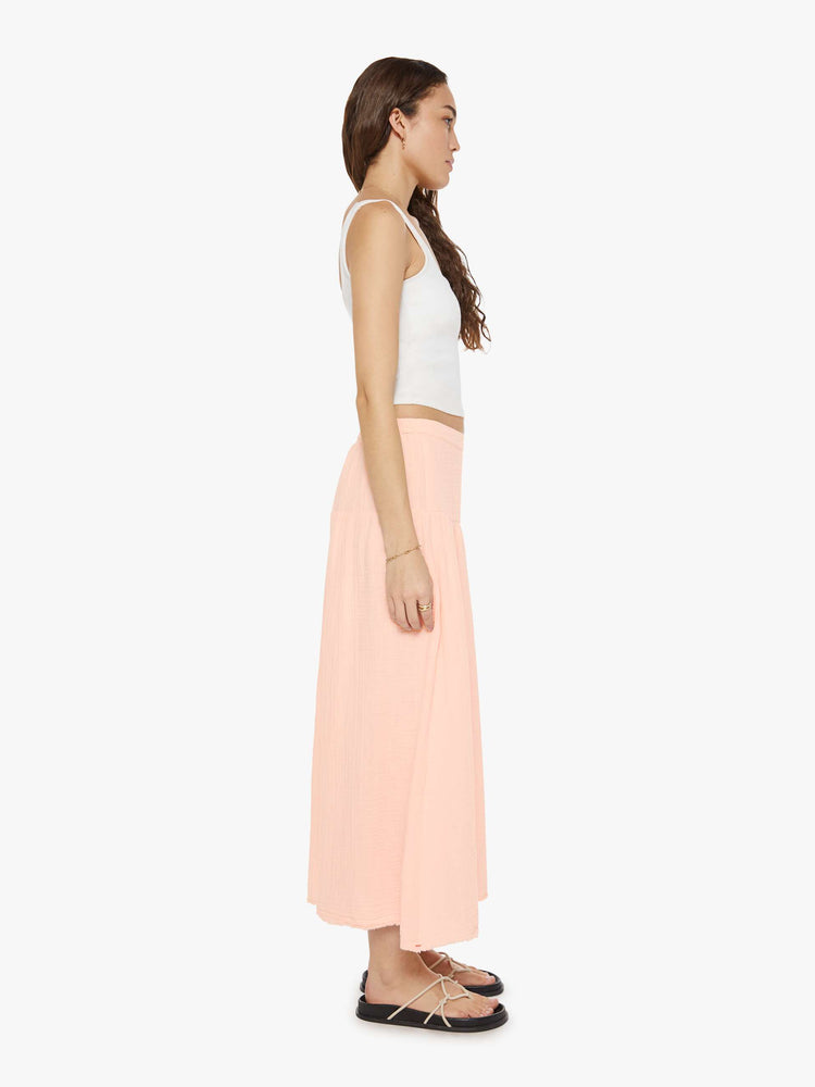 Side view of a woman in pink a smocked elastic waist, high rise, flowy skirt and an ankle-length hem.