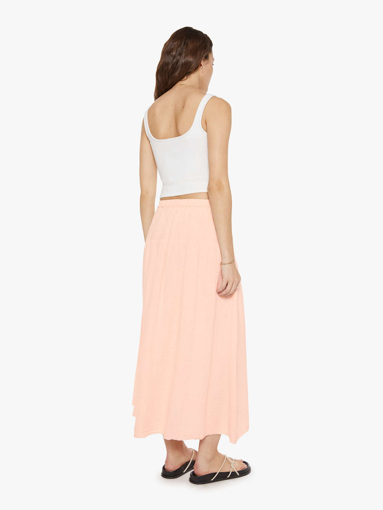 Back view of a woman in pink a smocked elastic waist, high rise, flowy skirt and an ankle-length hem.